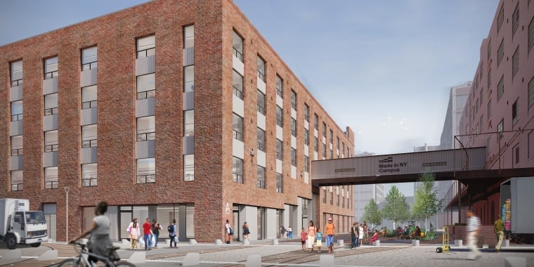 Modern brick building with large windows stands along a New York City street. People walk and gather outside, and a cyclist passes in the foreground. A sign overhead reads, “Made in NY Campus.” Trees and benches line the area.