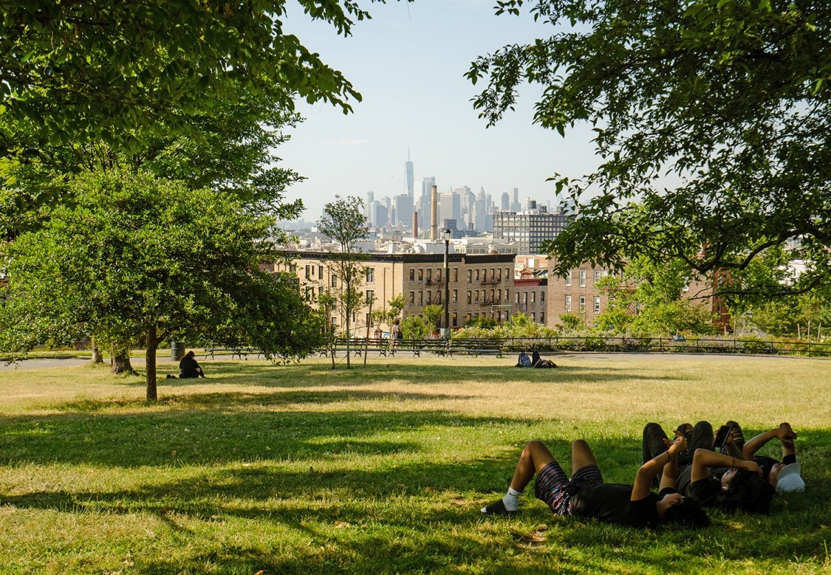 People relaxing on the grass in Sunset Park with trees and a city skyline in the background on a sunny day. People relaxing on the grass in Sunset Park with trees and a city skyline in the background on a sunny day.